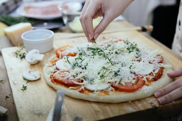 A chef sprinkles mozzarella on a pizza